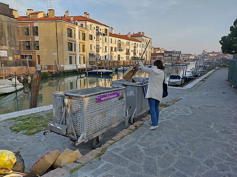 Photo of a woman dropping a bag of garbage in a cart at a garbage collection point in Venice.