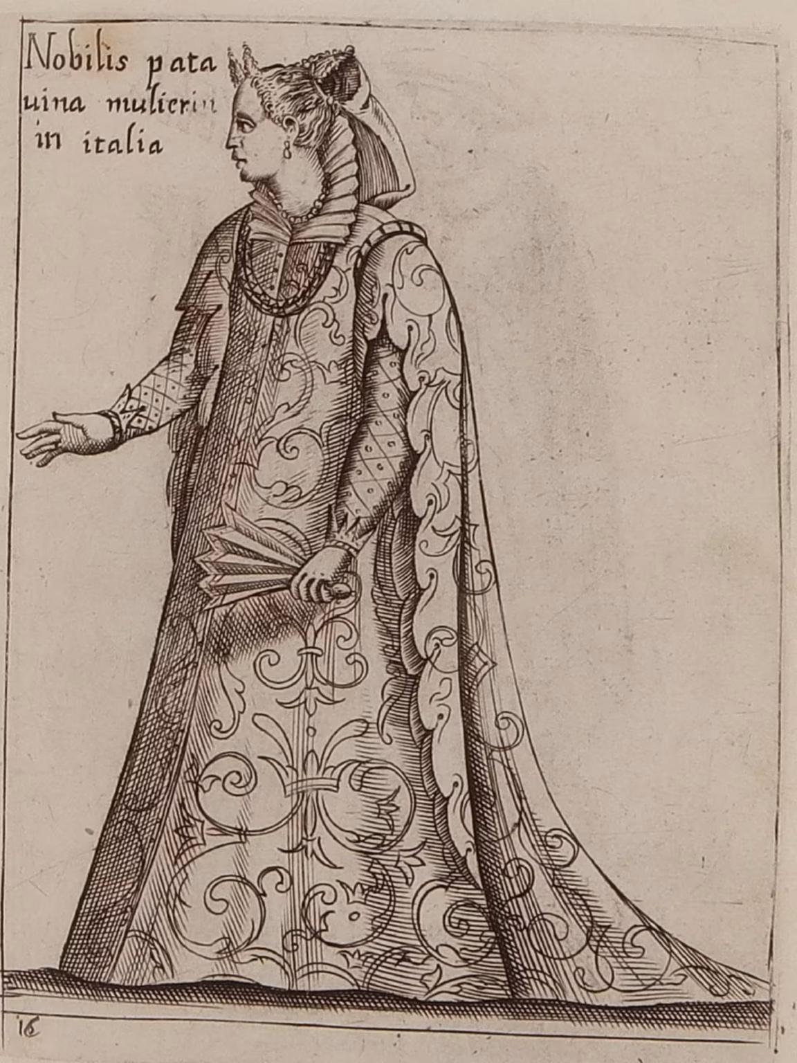 A monochrome print of a Paduan noblewoman, dressed in a long gown of fine brocade, with a matching cape. She wears a stiffened lace collar, a pearl necklace, and holds a foldable fan in one hand. Her hair is set as two horns, in the particular Venetian style.